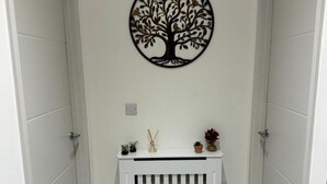 A hallway with a wall-mounted tree decoration, a small white console table with decorative items, and a white radiator.