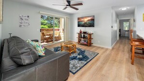 A spacious living room with a leather couch, a blue patterned rug, a wooden coffee table, and a ceiling fan.