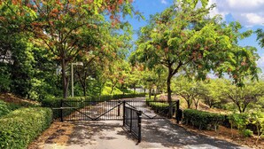 A gated pathway leading into a park with trees and a clear sky.