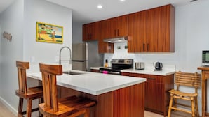 A modern kitchen with wooden cabinets, a stainless steel refrigerator, and a central island with bar stools.