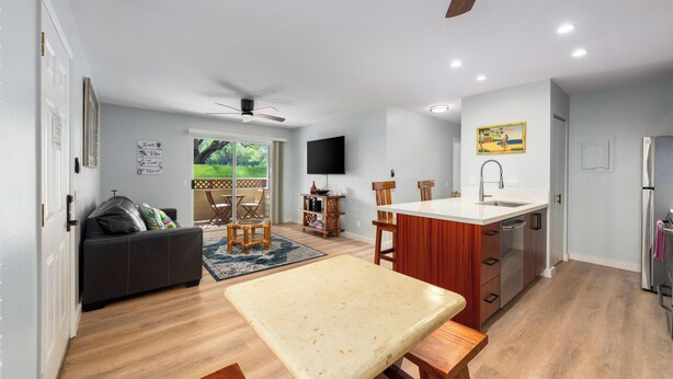 A modern kitchen with a central island, a dining area with a table and chairs, a sofa, and a TV mounted on the wall.