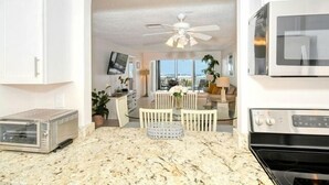 A kitchen with a granite countertop, a built-in oven, and a microwave. There is a dining area with a table and chairs, and a ceiling fan above. - Gulf Views 2 Bed 2 Bath at Siesta Key Beach 100 Steps to the Sand (Siesta Key)