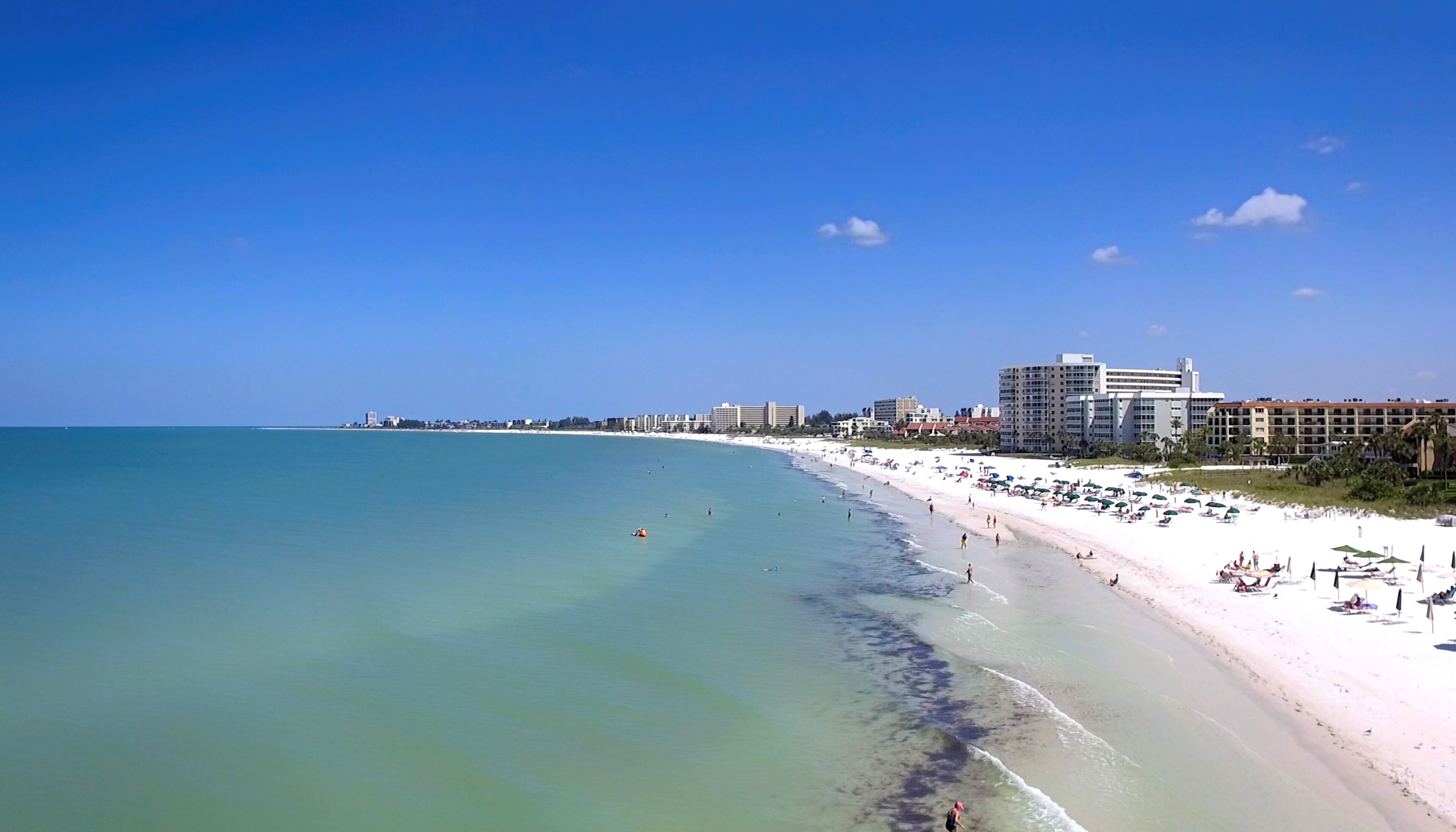 A beach with a wide sandy shore, clear blue water, and a row of hotels along the coastline.