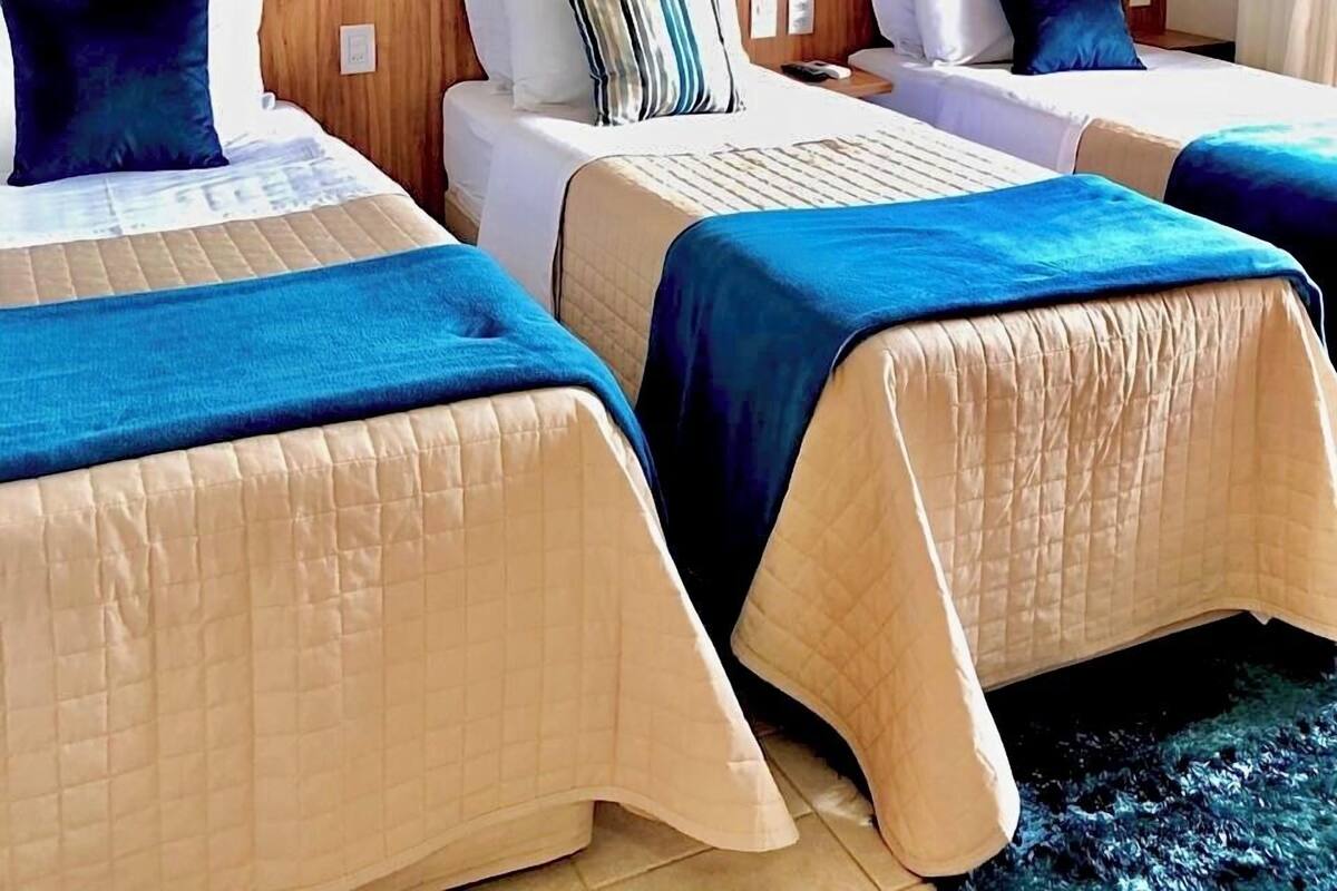 Ein Hotelzimmer mit zwei Betten, jeweils mit blauer und beige farbener Bettdecke, weißen Kissen und einem Holz-Kopfschild.