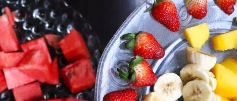 Uma fatia de bolo com cobertura branca e um prato de frutas fatiadas, incluindo morangos e bananas.