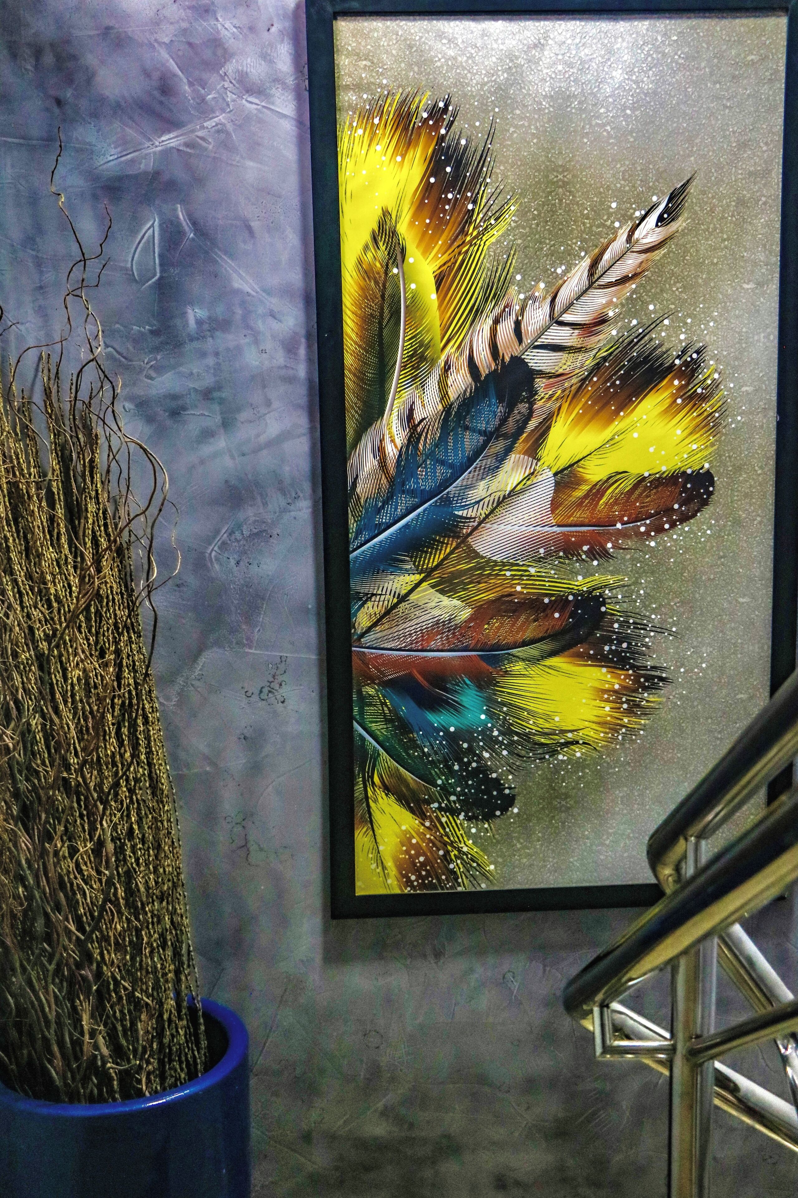 Obra de arte emoldurada com penas coloridas na parede.