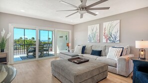 A spacious living room with a large window, a ceiling fan, a sofa set, and a coffee table.