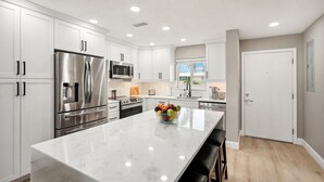 Una cocina moderna con armarios blancos, electrodomésticos de acero inoxidable e isla de mármol.