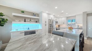 A modern kitchen with white cabinetry, a marble countertop, and a built-in island with a fruit bowl.