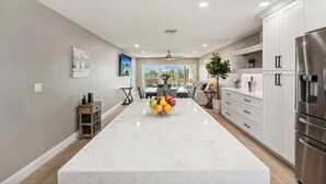 Una cocina moderna con armarios blancos, encimera de mármol y refrigerador de acero inoxidable.