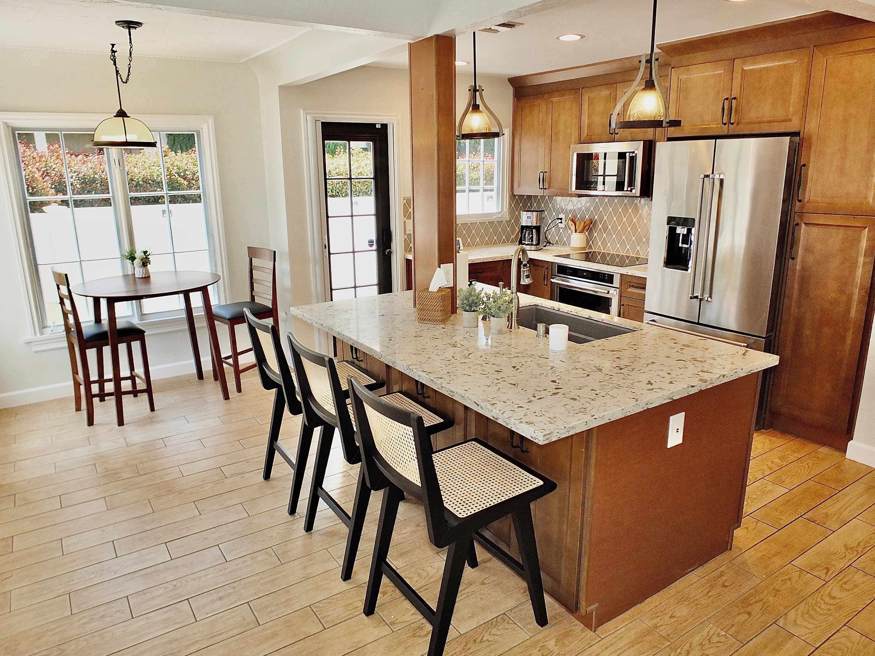 A modern kitchen with a large island, wooden cabinets, stainless steel appliances, and a dining area with chairs and a table.