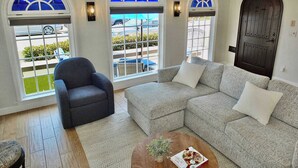 A living room with a grey armchair, a patterned sofa, and a coffee table with a book and a plant. - Belmont Shore Beach House (Long Beach)