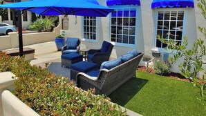 A patio with wicker furniture and blue cushions, a large potted plant, and a blue umbrella. - Belmont Shore Beach House (Long Beach)