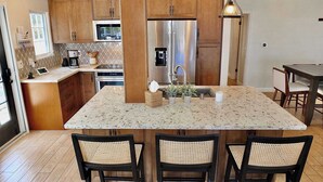 A modern kitchen with wooden cabinets, stainless steel appliances, a central island with seating, and a dining area. - Belmont Shore Beach House (Long Beach)