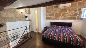 A bedroom with a bed, a wooden floor, a stone wall, and a balcony with a railing. - Alghero my Love (Alghero)