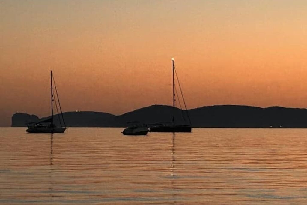 Dos veleros sobre aguas tranquilas, con un atardecer de fondo.