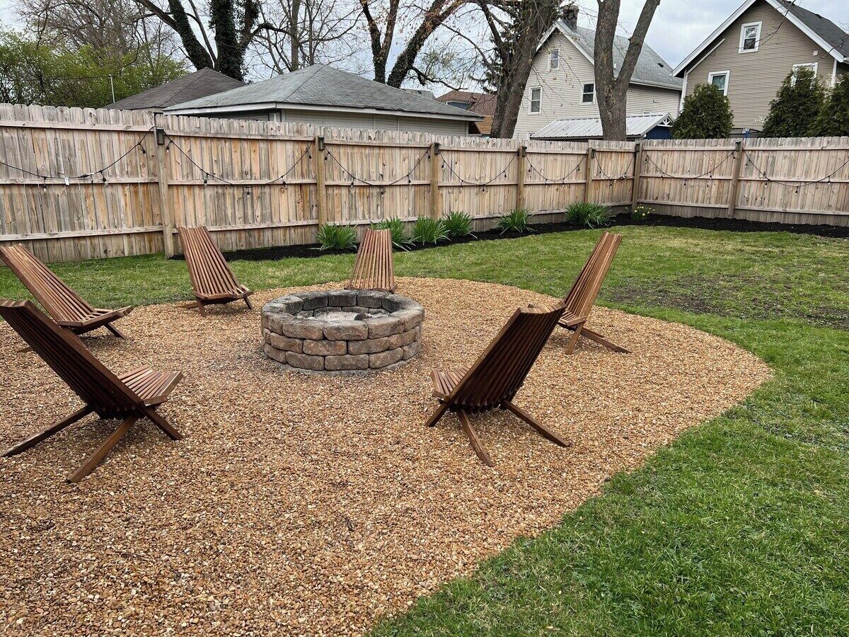 A backyard with a fire pit, four wooden chairs, and a wooden fence.
