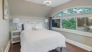 A bedroom with a large bed, a ceiling fan, and a window with a view of trees.