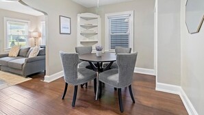 A dining area with a round table and four chairs, a ceiling fan, and a window with blinds.