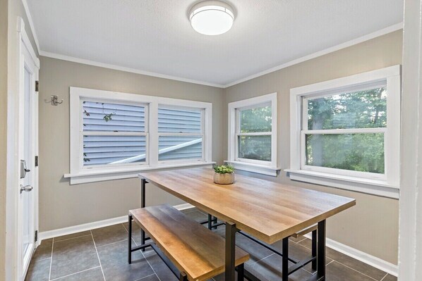 A dining area with a wooden table and bench, two windows with blinds, and a ceiling light.
