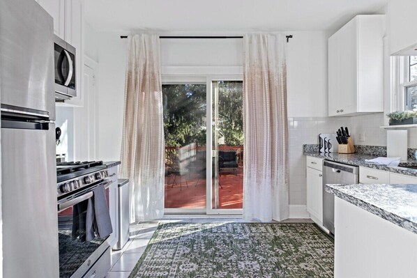 Cocina moderna con armarios blancos, estufa de acero inoxidable y puerta corrediza de vidrio que da a un patio.