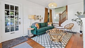 A living room with a green sofa, wicker chairs, a patterned rug, and a staircase. - Peaceful Oakley Escape 2bd|Lg Priv Deck w views (Cincinnati)