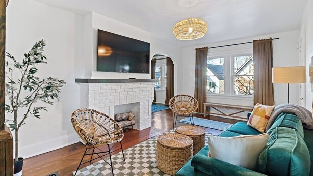 A living room with a fireplace, wicker chairs, a green sofa, and a large TV. - Peaceful Oakley Escape 2bd|Lg Priv Deck w views (Cincinnati)