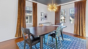 A dining area with a dark wooden table, four chairs, a blue patterned rug, and brown curtains. - Peaceful Oakley Escape 2bd|Lg Priv Deck w views (Cincinnati)