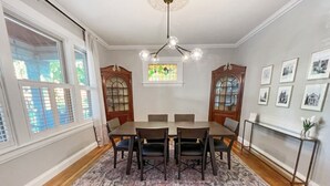 Une salle à manger avec une table et des chaises en bois, un tapis à motifs et un lustre.