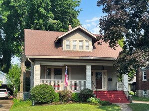 A two-story house with a front porch, a flag, and a red front door.