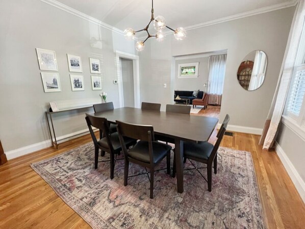 A dining room with a large table, six chairs, and a patterned rug.
