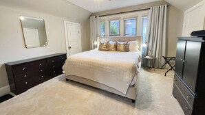 Une chambre à coucher comprenant un lit, une commode, un ventilateur de plafond et une fenêtre avec des rideaux.