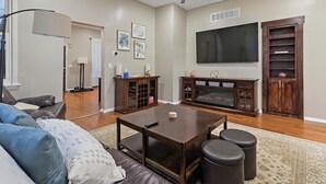 Uma sala de estar com sofá, mesa de centro, pufes, TV, centro de entretenimento e lareira.