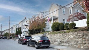 Uma rua residencial com casas, um muro de pedra e carros estacionados.