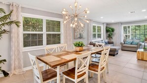 A spacious living area with a dining table, chairs, a sofa, and a chandelier.
