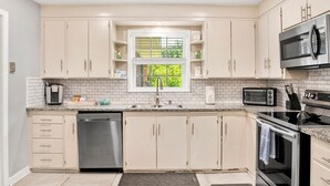 A modern kitchen with white cabinets, a stainless steel dishwasher, a microwave, and an oven.