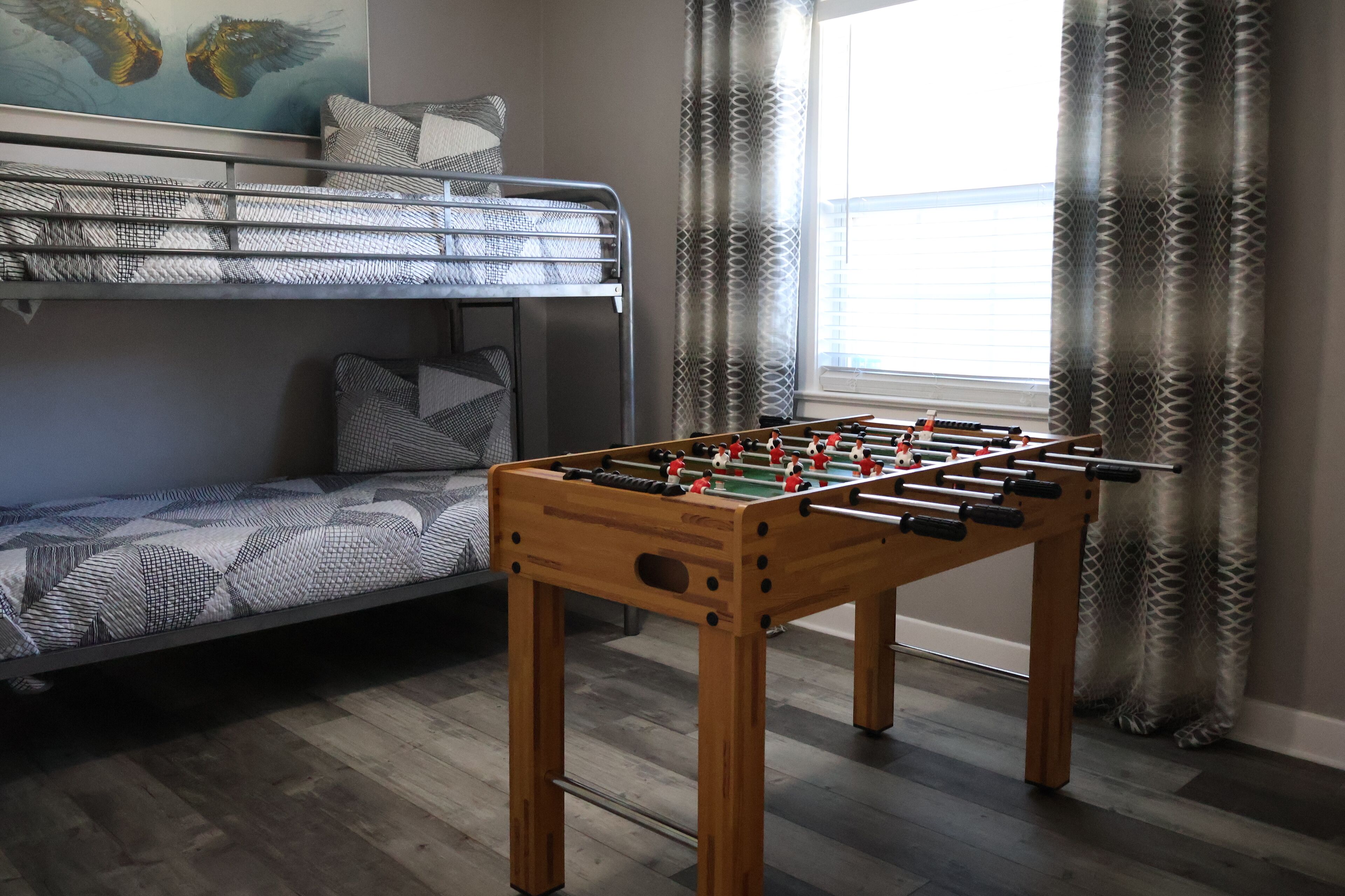 Een kamer met een stapelbed, een tafelvoetbalspel en een raam met gordijnen met een patroon.