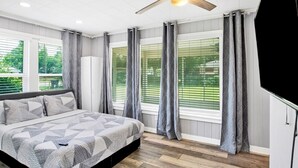 A bedroom with a bed, a ceiling fan, and large windows with curtains.