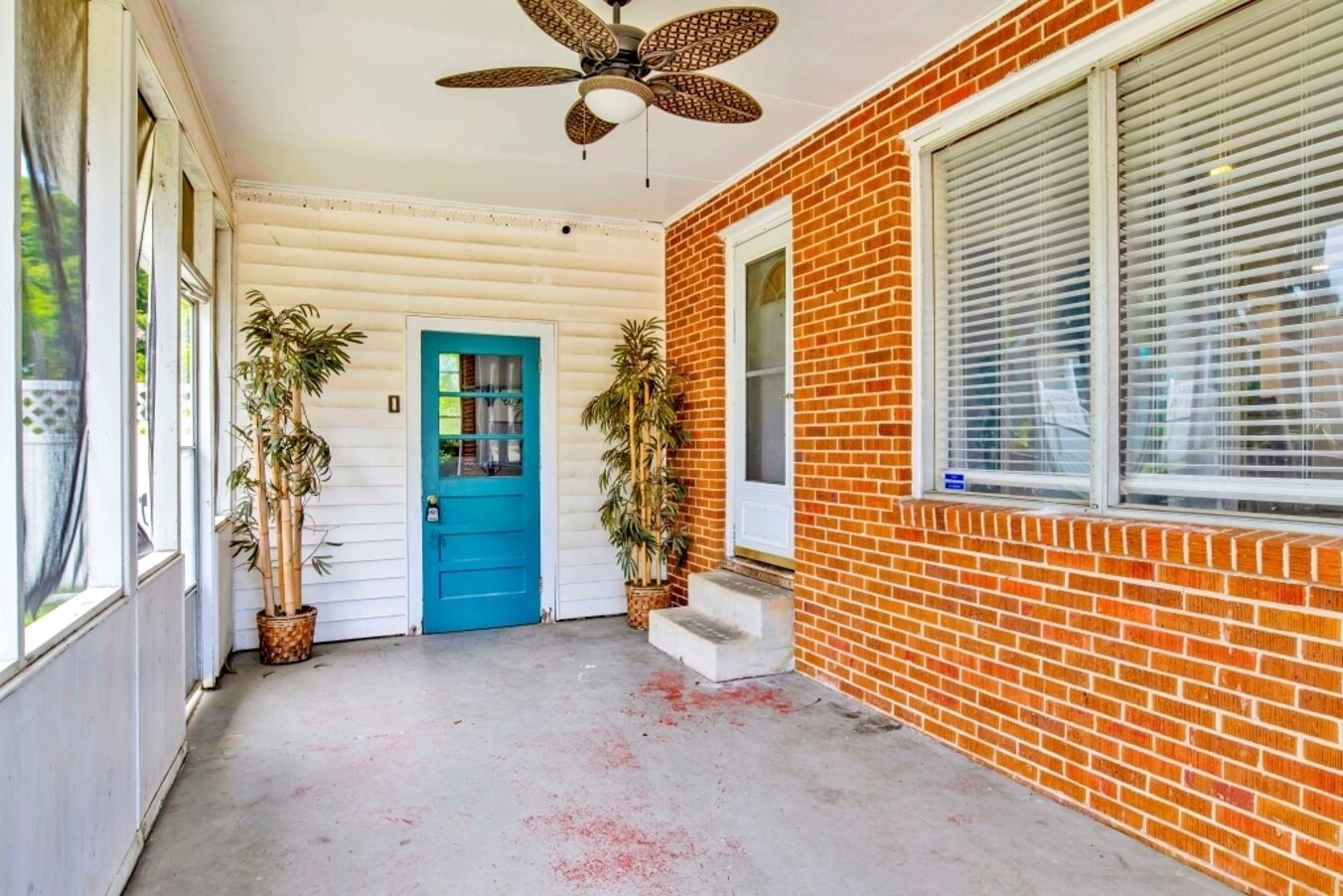 A covered porch with a blue door, potted plants, and a ceiling fan.