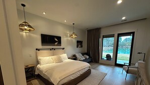 A bedroom with a large bed, a view of a swimming pool, and a chair by the window. - Egret Cottage Suite    3715-B (WALTERBORO)