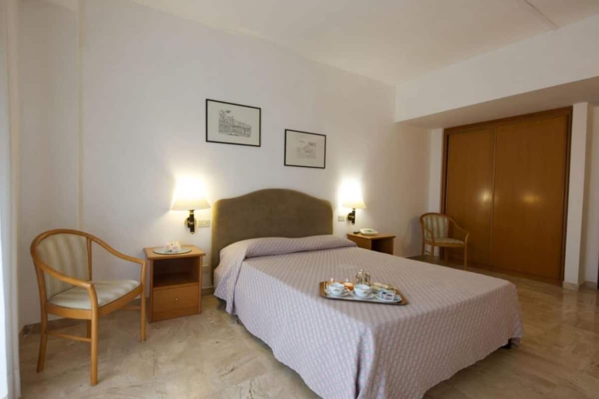 A hotel room with a bed, two bedside tables, two lamps, a chair, and a wardrobe.