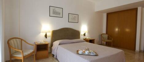 Una habitación de hotel con una cama, dos mesitas de noche, dos lámparas, una silla y un armario.