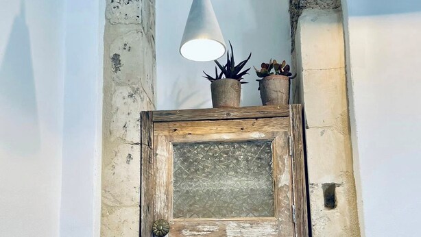 Eine Küche mit rustikaler Steinwand, einem Holzkabinett mit Glastür, einem Waschbecken mit modernem Wasserhahn und einer Pendelleuchte darüber.