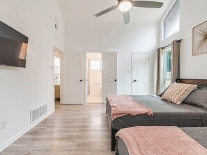 A bedroom with two beds, a ceiling fan, a TV, and a window with curtains.