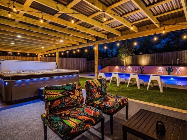 An outdoor patio area with a hot tub, colorful chairs, and a wooden ceiling structure.