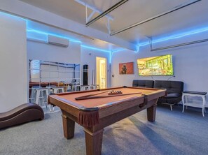 A pool table in a room with a sofa and a television.