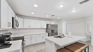 A modern kitchen with white cabinetry, stainless steel appliances, a central island with stools, and recessed ceiling lighting. - Contemporary 3-Bed,2-Bath Home, Downtown WPB! (West Palm Beach)