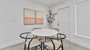 A dining area with a round table, four chairs, two abstract paintings, a potted plant, and a white door. - Contemporary 3-Bed,2-Bath Home, Downtown WPB! (West Palm Beach)