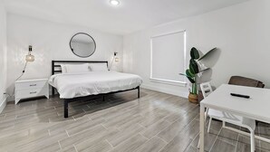 A modern bedroom with a bed, bedside tables, a mirror, a potted plant, and a white desk with a remote control. - Contemporary 3-Bed,2-Bath Home, Downtown WPB! (West Palm Beach)