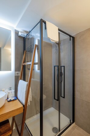 Une salle de bain moderne avec une douche à parois de verre, une échelle en bois et un lavabo blanc agrémenté d’articles de toilette.